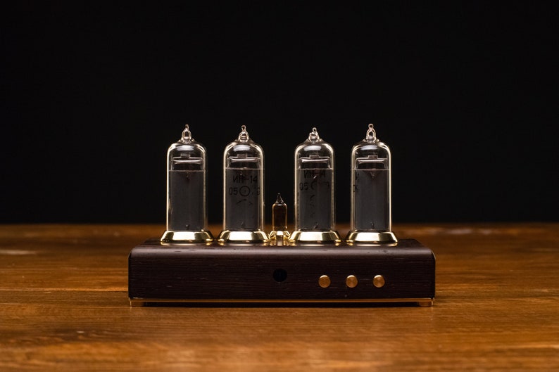 Puede incluir: Un reloj de estilo vintage con cuatro tubos Nixie de vidrio transparente que muestran la hora. El reloj est&aacute; montado sobre una base de madera oscura con detalles dorados.