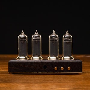 May include: A four-digit clock with clear glass tubes and a dark wood base. The tubes are lit up with a dark gray color, and the base has a gold trim.