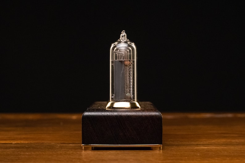 May include: A clear glass Nixie tube clock with a gold base and a dark wood frame. The tube is lit up and displaying the number 1.