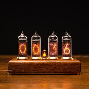 Puede incluir: Un reloj de madera con cuatro tubos Nixie que muestran la hora 00:36. Los tubos est&aacute;n iluminados con un c&aacute;lido brillo naranja.