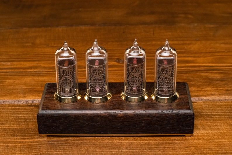 May include: A vintage-style clock with four clear glass Nixie tubes displaying the time. The tubes are mounted on a dark wood base with brass accents.