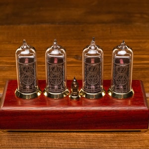 Puede incluir: Un reloj de estilo vintage con cuatro tubos Nixie de vidrio transparente que muestran la hora. El reloj est&aacute; montado sobre una base de madera roja oscura con detalles dorados.