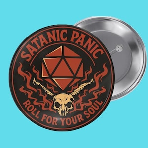 Peut inclure: Un bouton de 5,7 cm de diamètre avec l'inscription "SATANIC PANIC" et "ROLL FOR YOUR SOUL". Le design comprend une forme géométrique, des flammes et une tête de mort. Le bouton est noir, rouge et argenté, sur fond bleu clair.