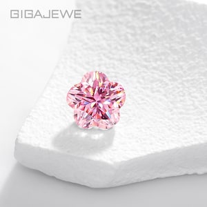 May include: A pink, flower-shaped gemstone with multiple facets, set against a white, textured surface. The gemstone has a star-like centre and is labelled with the brand name "GIGAEWE" at the top.