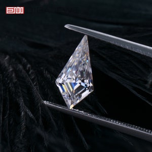 May include: A clear, faceted, diamond-shaped gemstone with a pointed top, held by a pair of tweezers against a black background.