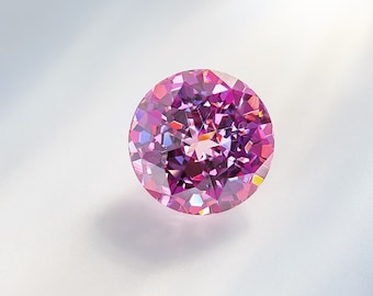 May include: A round, faceted gemstone with a pink and purple hue. The gemstone is set against a white background.