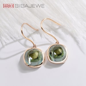 May include: A pair of gold earrings with green gemstone drops. The earrings have a square shape and a hook closure.