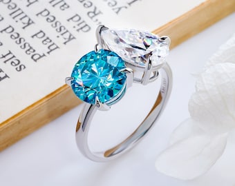 May include: A silver ring with a blue round gemstone and a clear pear-shaped gemstone.