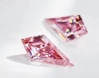 Può includere: Due pietre preziose rosa, sfaccettate, di forma triangolare. Le pietre preziose sono su una superficie bianca.
