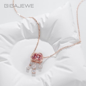 Könnte beinhalten: Eine roségoldene Halskette mit einem wolkenförmigen Anhänger, der einen großen rosa Edelstein und drei hängende Anhänger mit kleinen klaren Steinen aufweist. Der Text GIGAJEWE ist oben links zu sehen. Die Kette ist sehr fein gearbeitet.