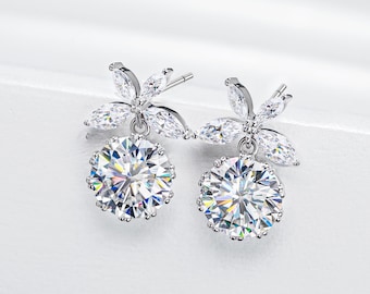 May include: A pair of silver earrings with a flower design and a large round clear crystal. The earrings are dangling and have a delicate look.