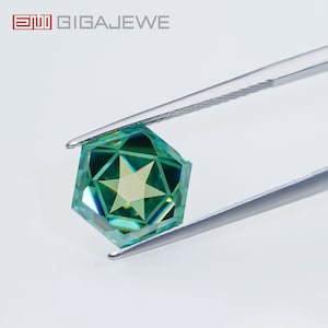 May include: A green gemstone with a star-shaped pattern is held by tweezers. The gemstone is cut into a hexagonal shape with many facets. The background is white.