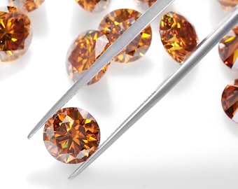 May include: A collection of faceted, round, orange-brown gemstones. One gem is held by silver tweezers, showcasing its brilliant cut. Other gems are scattered around, reflecting light. The gems are on a white surface.