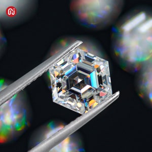 May include: A clear, square-shaped diamond with a complex, faceted design, held by tweezers against a black background with out-of-focus, iridescent circles.