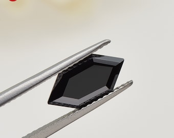 May include: A black hexagonal gemstone held by tweezers. The gemstone is faceted and has a high polish.