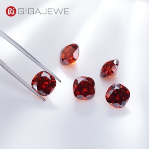 May include: Five loose red cushion-cut gemstones on a white surface. The gemstones are being held by tweezers.
