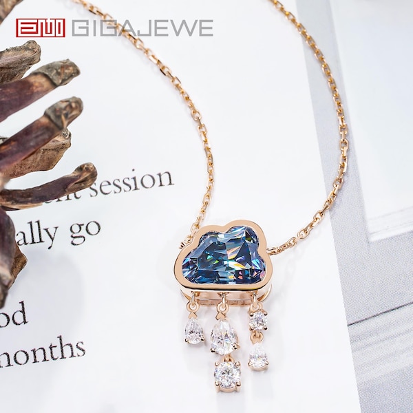 Può includere: Una delicata collana a catena dorata con un ciondolo a forma di nuvola con una pietra preziosa blu e una fila di pietre preziose trasparenti pendenti. La collana è su una superficie bianca con testo sullo sfondo.