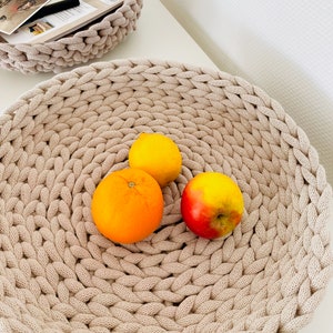 K&ouml;nnte beinhalten: Eine beige geh&auml;kelte Schale mit einer Zitrone, einer Orange und einem roten Apfel.