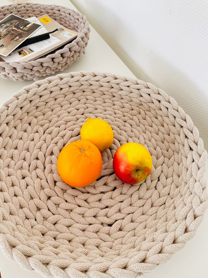 K&ouml;nnte beinhalten: Eine beige geh&auml;kelte Schale mit einer Zitrone, einer Orange und einem roten Apfel.