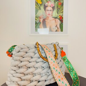 May include: A gray knitted tote bag with a bamboo handle and a colorful patterned strap. The strap is orange, green, and white with a geometric design.