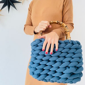 Könnte beinhalten: Eine blaue Stricktasche mit einem Bambusgriff. Die Tasche ist aus dickem, grobem Garn gefertigt und hat eine gewebte Textur.