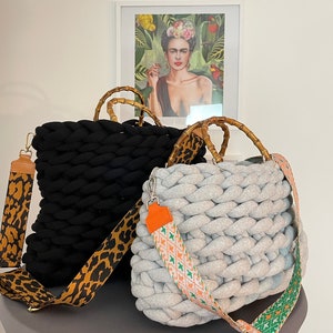 May include: Two knitted tote bags with bamboo handles. One bag is black with a leopard print strap, the other is gray with a colorful geometric strap.