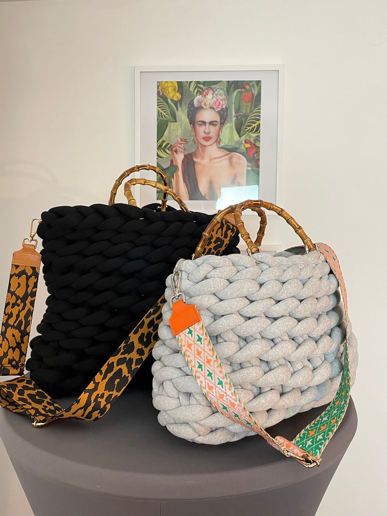 May include: Two knitted tote bags with bamboo handles. One bag is black with a leopard print strap, the other is gray with a colorful geometric strap.