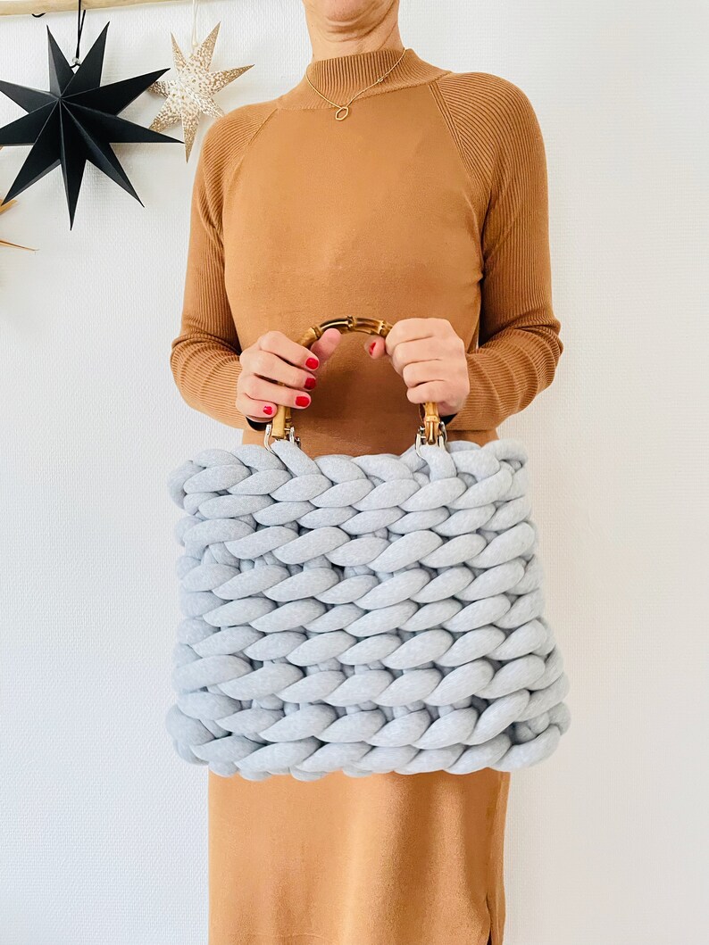 May include: A light gray knitted tote bag with a bamboo handle. The bag is made with thick, chunky yarn and has a square shape.