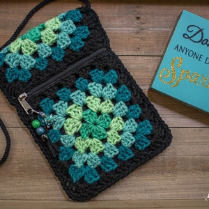 Może przedstawiać: Czarna szydełkowa torba na ramię z wzorem granny square w odcieniach zieleni i turkusu. Torba ma zapięcie na zamek błyskawiczny i czarny sznurkowy pasek. Na zdjęciu widoczny jest również drewniany znak z napisem "Don't Let Anyone Dull Your Sparkle".
