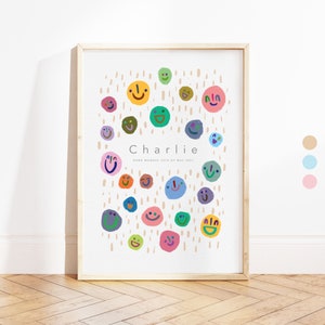 May include: A white framed print with a light brown background and colourful smiley faces. The text "Charlie" is in black and the text "Born Monday 24th of May 2021" is in grey.