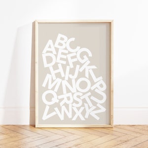 May include: A framed print with a beige background and white letters spelling out the alphabet in a random order.