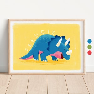 May include: A yellow watercolour background with a blue triceratops dinosaur with a pink mouth and white horns. The name "FREDDIE" is written in white letters on the background.