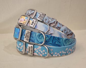 May include: Three pet collars with silver buckles and metal tags. The top collar has a blue and brown marble pattern with the text Pepper 123-456-7890 987-654-3210. The middle has a blue swirl pattern with Stuart 123-456-7890 987-654-3210. The bottom has pink flowers with Penny 123-456-7890.