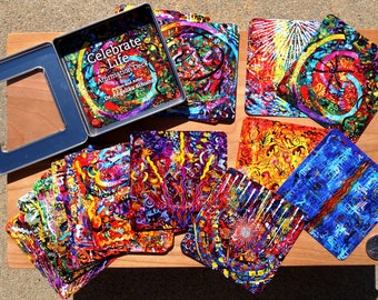 May include: A set of colourful affirmation cards in a metal tin. The cards feature abstract art with bright colours and swirling patterns. The tin has the words "Celebrate Life Affirmation Deck" printed on it.
