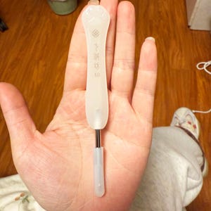 Puede incluir: Un ganchillo blanco con un mango decorativo con un diseño de huella de pata y texto japonés. El ganchillo tiene un eje de metal plateado y una punta de plástico transparente. El mango tiene el número 4.0.