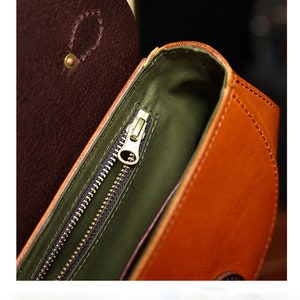 May include: Close-up of the inside of a brown leather bag with a gold zipper. The bag has a green lining.