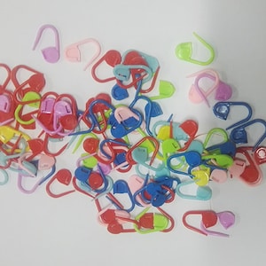 Könnte beinhalten: Ein großer Haufen bunter Plastik-Maschenmarkierer in verschiedenen Formen und Größen. Die Markierer sind in Rot-, Rosa-, Blau-, Grün- und Gelbtönen.