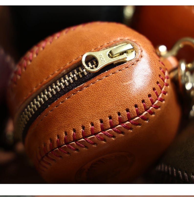 May include: A brown leather baseball-shaped zippered pouch with red stitching. The zipper is open and the pouch is empty.