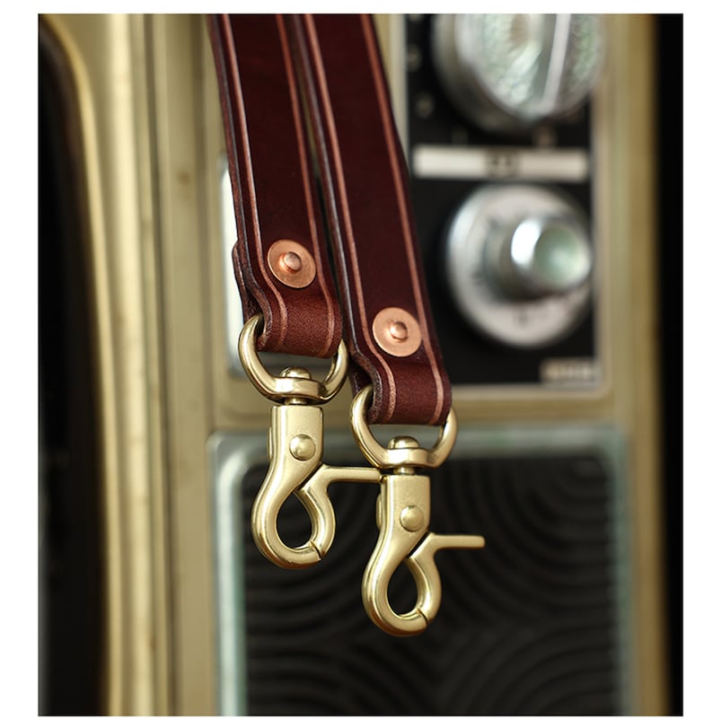 May include: Two brown leather straps with copper rivets and brass swivel clasps.