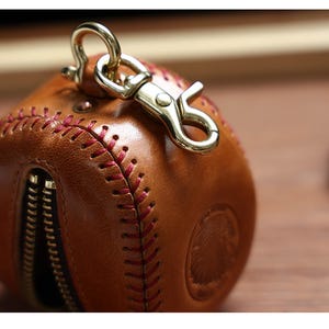 May include: A brown leather baseball-shaped keychain with red stitching and a gold metal clasp.
