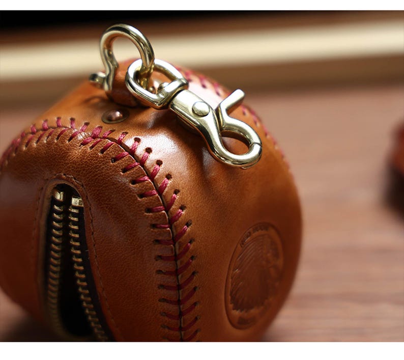 May include: A brown leather baseball-shaped keychain with red stitching and a gold metal clasp.