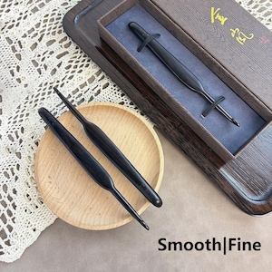 May include: Two black wooden crochet hooks with smooth, tapered handles resting on a small round wooden plate, alongside a matching hook secured inside a dark brown rectangular presentation box with gold text and a blue velvet interior lining.
