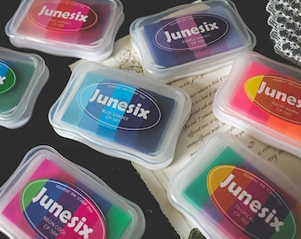 Pode incluir: Seis recipientes de plástico transparente com almofadas de tinta coloridas no interior. Cada almofada tem um esquema de cores diferente e diz "Junesix" com o nome da cor e o código. As cores são rosa, roxo, azul, laranja, verde e vermelho.
