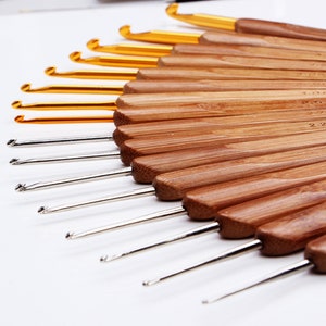 May include: A set of 15 bamboo crochet hooks with gold and silver tips. The hooks are arranged in a fan shape, with the largest hook at the top and the smallest hook at the bottom. The hooks are numbered 2.00, 2.25, 2.50, 2.75, 3.00, 3.25, 3.50, 3.75, 4.00, 4.50, 5.00, 5.50, 6.00, 6.50, 7.00.