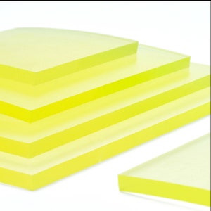 May include: Stack of four translucent yellow rectangular sheets of rubber. The sheets are stacked in a pyramid shape, with the largest sheet at the bottom and the smallest sheet at the top. A smaller sheet of rubber is in the foreground.