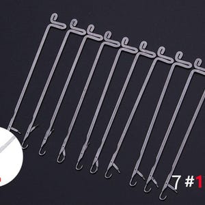 May include: A set of 10 silver-colored metal knitting machine needles, each featuring a latch hook mechanism at the tip and a looped handle at the top. A circular inset shows a close-up of the needle tip with a 3mm measurement label.