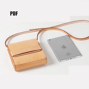 May include: A light brown leather crossbody bag with a flap closure and a small pocket on the front. The bag is shown with a silver iPad.