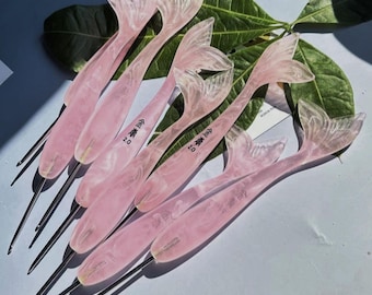 May include: A collection of crochet hooks with translucent, marbled pink handles shaped like mermaid tails. Each handle features a metallic hook tip and is imprinted with the text '金誉 2.0'. The hooks are arranged in a fan-like pattern.