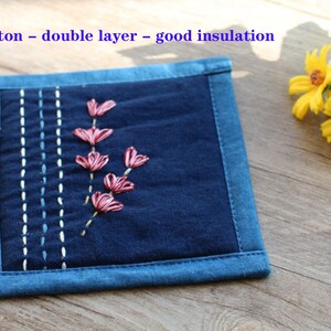 Puede incluir: Un posavasos de algod&oacute;n azul de doble capa con flores bordadas de color rosa. El texto "Cotton - double layer - good insulation" est&aacute; impreso en la parte superior de la imagen.