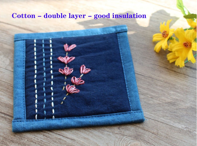 Puede incluir: Un posavasos de algod&oacute;n azul de doble capa con flores bordadas de color rosa. El texto "Cotton - double layer - good insulation" est&aacute; impreso en la parte superior de la imagen.